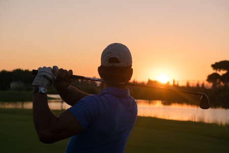 golfer hitting long shot with driver on course at beautiful sunsetの写真素材