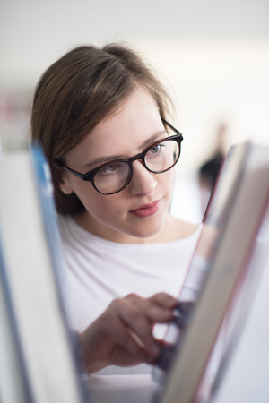 portrait of smart looking famale student girl  in collage school library,  selecting book to read from bookshelfの写真素材
