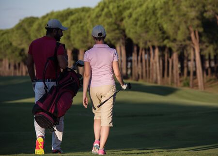 young couple walking to next hole on golf course. man carrying golf bagの写真素材