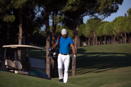 handsome middle eastern golfer  carrying  bag  and walking  to next hole at golf  courseの写真素材