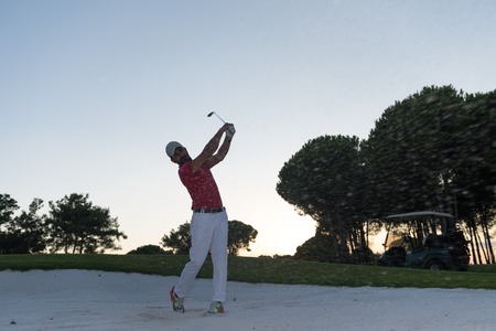golf player shot ball from sand bunker at course with beautiful sunset with sun flareの写真素材