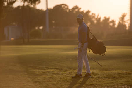handsome middle eastern golfer  carrying  bag  and walking  to next hole at golf  course on beautiful sunset in backgroundの写真素材