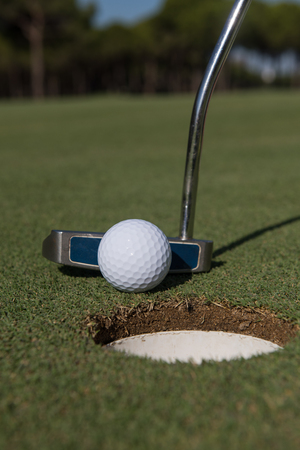 close up of putter hitting golf ball to hole at courseの写真素材