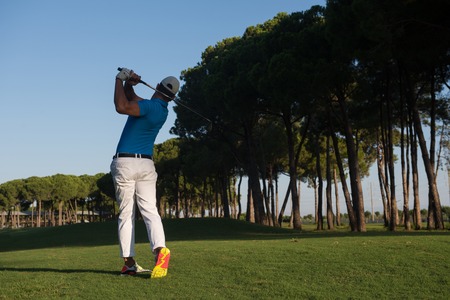 handsome sporty man, golf player hitting shot with club on course at beautiful morningの写真素材