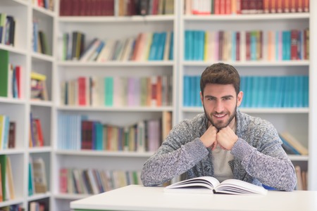 Portrait of happy student while reading book in school library. Study lessons for  exam. Hard worker...