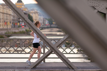 sporty woman running on sidewalk at early morning with city  sunrise scene in backgroundの写真素材