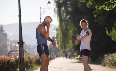 jogging couple check music playlist on phone and plan route before morning running workout  with sunrise in the city  and sun flare in backgroundの写真素材
