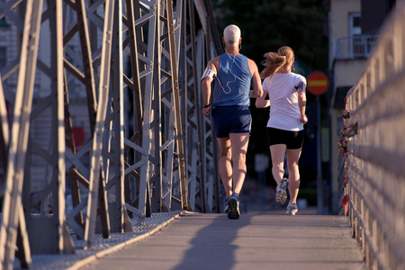 healthy mature couple jogging in the city  at early morning with sunrise in backgroundの写真素材