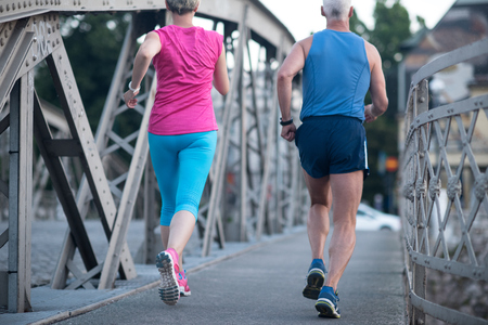 healthy mature couple jogging in the city  at early morning with sunrise in backgroundの写真素材