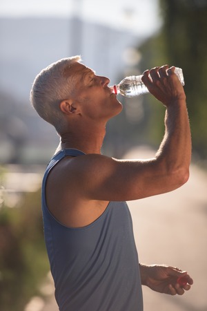 handsome senior jogging man drinking fresh water from bottle after mornig runの写真素材
