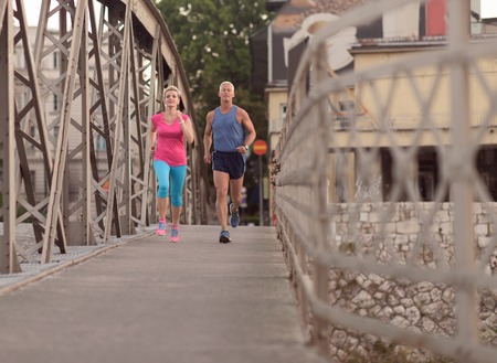 healthy mature couple jogging in the city  at early morning with sunrise in backgroundの写真素材