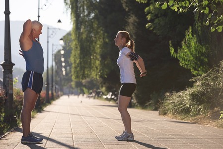 jogging couple warming up and stretching before morning running training workout  in the city with sunrise in backgroundの写真素材