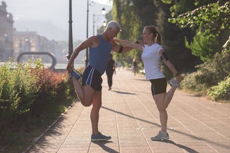 jogging couple warming up and stretching before morning running training workout  in the city with...