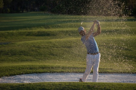 golfer shot ball from sand bunker at golf course with beautiful sunset in backgroundの写真素材