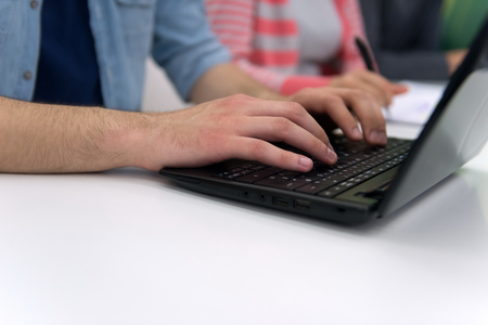 close up of young business man student student hands typing on laptop computer at modern school classroom, blured classmates in backgrondの写真素材