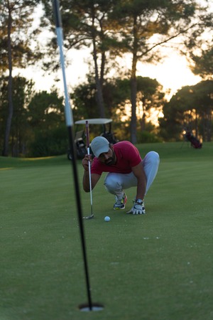 golf player aiming shot with club on course at beautiful sunset with sun flare in backgroundの写真素材