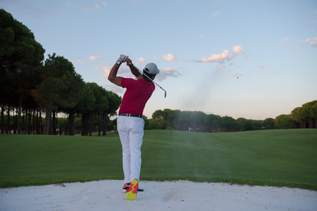 golf player shot ball from sand bunker at course with beautiful sunset with sun flareの写真素材