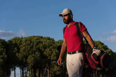handsome middle eastern golfer  carrying  golf bag  and walking at course to next holeの写真素材
