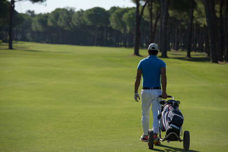 handsome middle eastern golf playerwalking with wheel bag at course on beautiful  sunny dayの写真素材