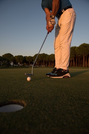 golfer hitting ball shot with driver on golf course at beautiful sunset in backgroundの写真素材
