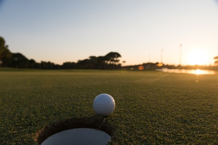 golf ball on edge of course hole representing achivement and success business concept, beautiful sunset in backgroundの写真素材