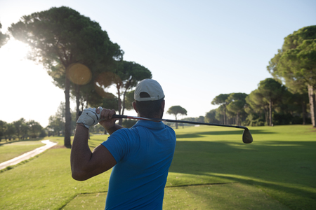 golf player hitting shot with club on course at beautiful morning with sun flare in backgroundの写真素材