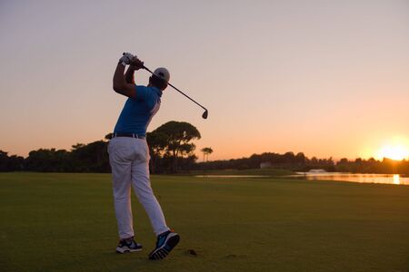 golfer hitting long shot with driver on course at beautiful sunsetの写真素材