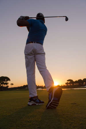 golfer hitting long shot with driver on course at beautiful sunsetの写真素材