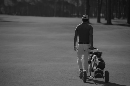handsome middle eastern golf playerwalking with wheel bag at course on beautiful  sunny dayの写真素材