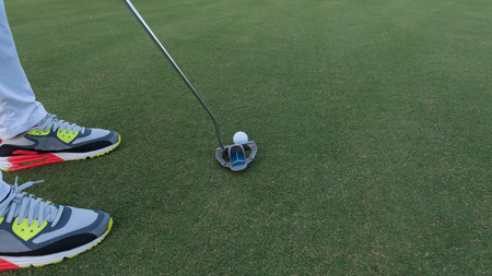 close up of putter hitting golf ball to hole at course