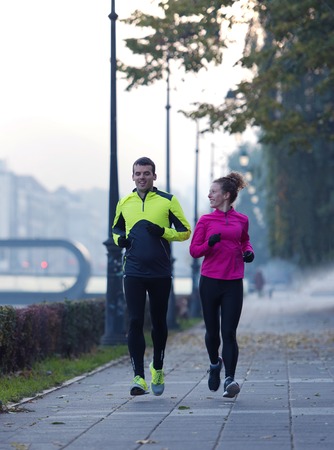 healthy young  couple jogging in the city  at early morning with sunrise in backgroundの写真素材
