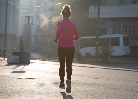 sporty woman running on sidewalk at early morning jogging with city  sunrise scene in backgroundの写真素材