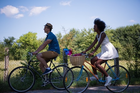 a young man and a beautiful African American girl enjoying a bike ride in nature on a sunny summer...