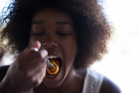 young beautiful African American woman enjoys while eating delicious pastaの写真素材