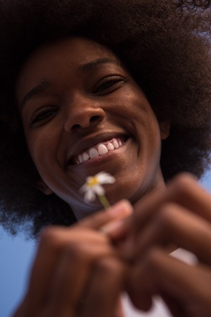portrait of a young beautiful African American girl with a flower of daisy in her hand