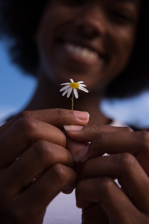 portrait of a young beautiful African American girl with a flower of daisy in her handの写真素材