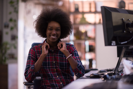 portrait of a young successful African American beautiful woman who enjoys spending a quality and joyful time while working in a large modern officeの写真素材