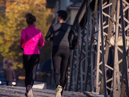 healthy young  couple jogging in the city  at early morning with sunrise in backgroundの写真素材