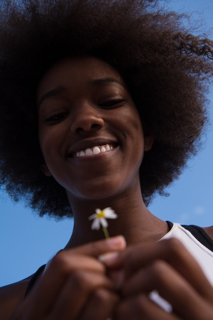 portrait of a young beautiful African American girl with a flower of daisy in her handの写真素材