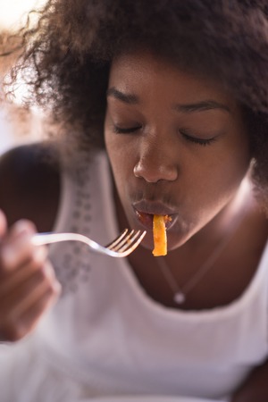 young beautiful African American woman enjoys while eating delicious pastaの写真素材