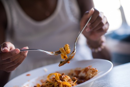 young beautiful African American woman enjoys while eating delicious pastaの写真素材