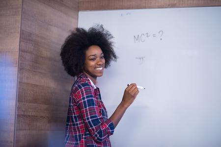 Young successful African American beautiful woman writes on a board meeting in a large modern office