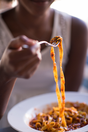 young beautiful African American woman enjoys while eating delicious pastaの写真素材