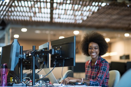 portrait of a young successful African American beautiful woman who enjoys spending a quality and joyful time while working in a large modern officeの写真素材