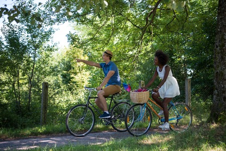 a young man and a beautiful African American girl enjoying a bike ride in nature on a sunny summer dayの写真素材