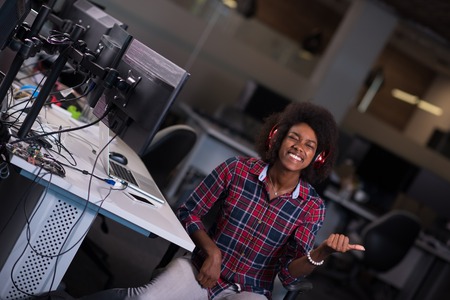 young black woman at her workplace in startup business office listening music on headphones and...