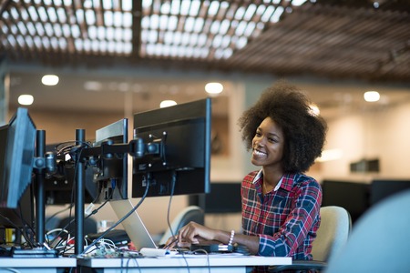 young black woman at her workplace in modern office  relaxing and working on laptop computer with dual monitor screenの写真素材