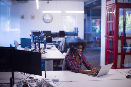 portrait of a young successful African American beautiful woman who enjoys spending a quality and joyful time while working in a large modern officeの写真素材