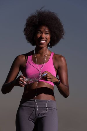 portrait of a young beautiful african american woman with headphones and a bottle of water after...