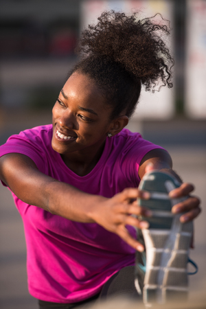 young beautiful African American woman doing warming up and stretching with her leg raised to the bridge before the morning run with the sunrise in the backgroundの写真素材